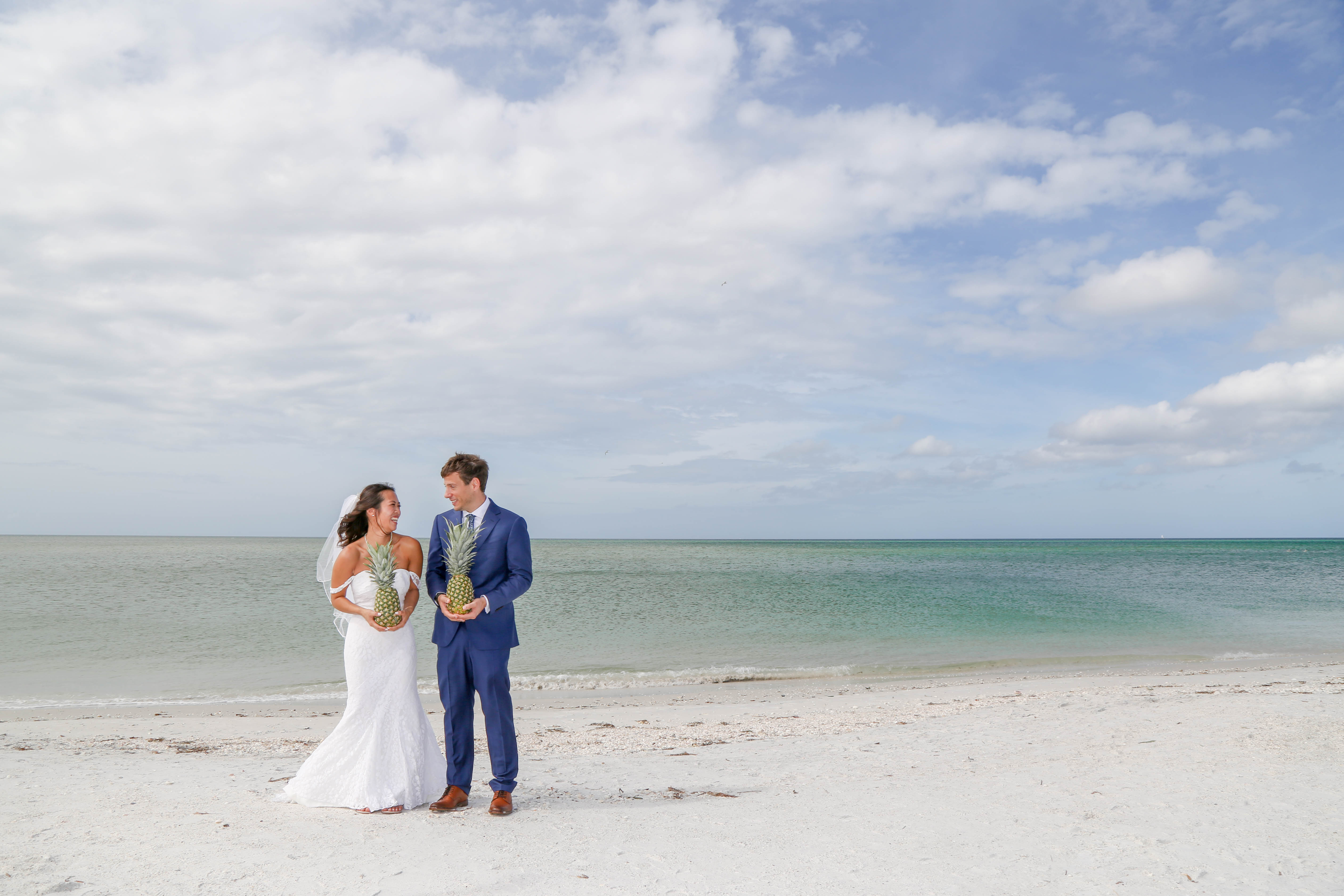 Bride and Groom on beach in Boca Grande holding pineapple