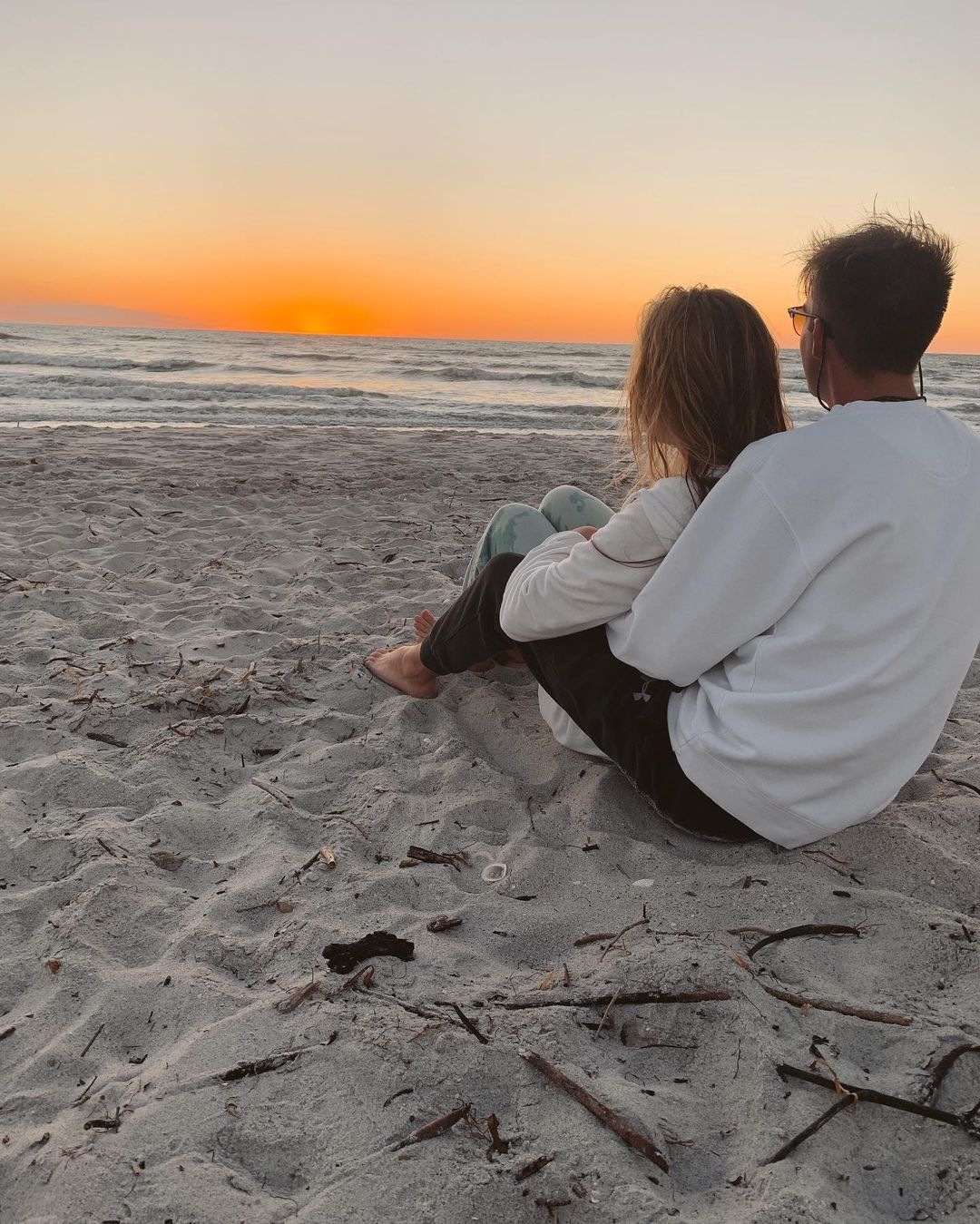 couple sitting on beach looking at the water as the sunsets