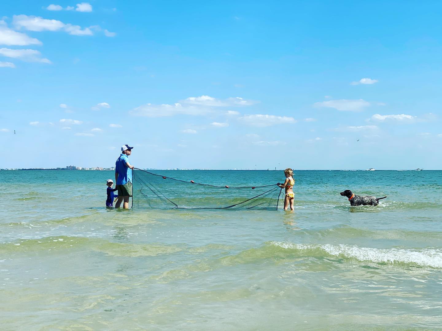 Two people throwing a cast net with dog nearby in the water.