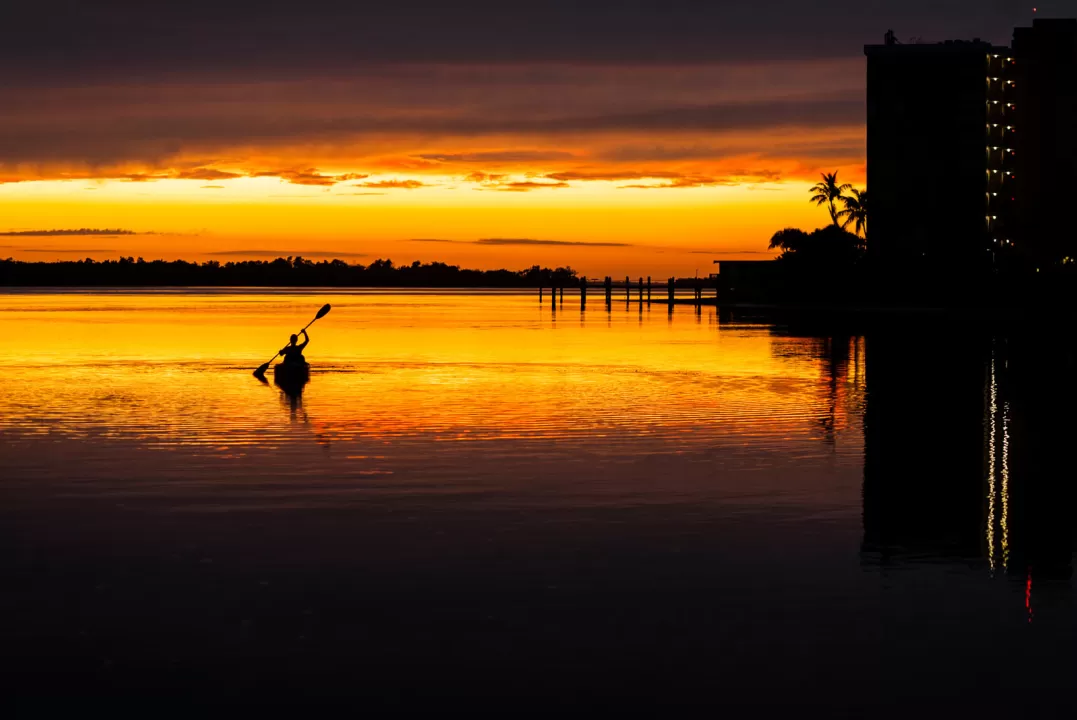 Silhouette eines einsamen Kajakfahrers, der bei einem pulsierenden Sonnenuntergang ans Ufer zurückkehrt