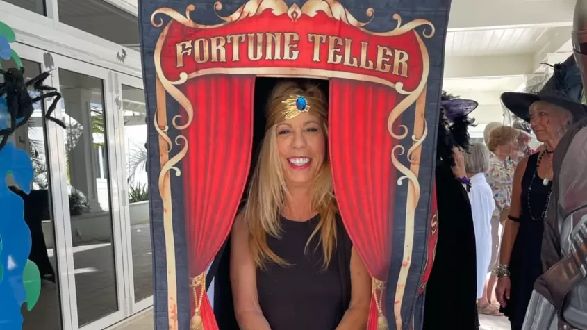 A woman dressed as a fortune teller in a fortune telling booth smiles