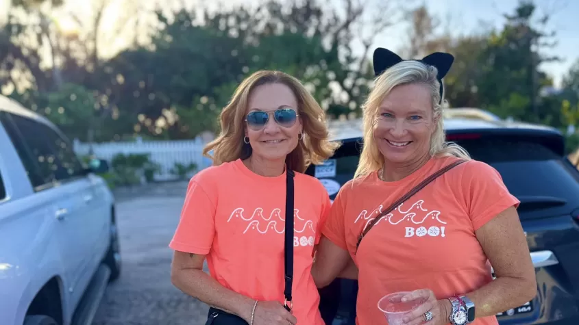 Two women smile with their arms around one another, dressed in matching bright orange t shirts the read "boo" with ghosts.