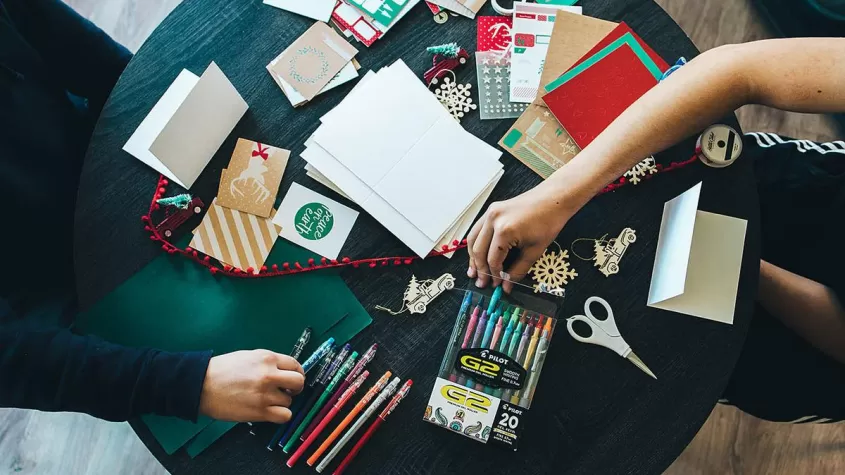 over head picture of people creating paper greeting cards on a green tablecloth