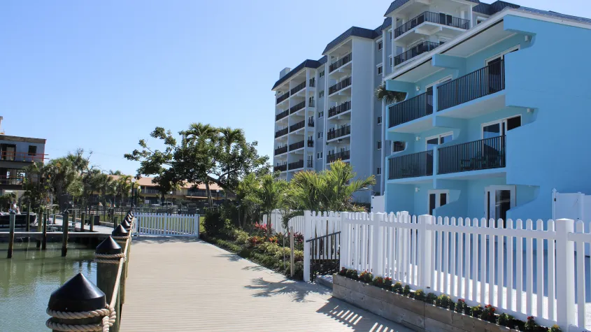 Bay inn  blue building exterior with large wooden dock, water, palm trees, white fence, and blue skies