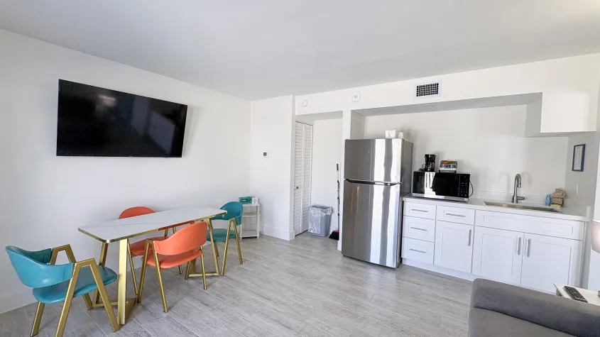 room viewing small kitchen, sink, cabinets, full refrigerator,  microwave, dining table and 4 chairs, tv