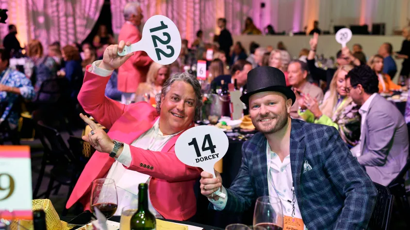 An event photo of a charity auction with two men holding auction paddles