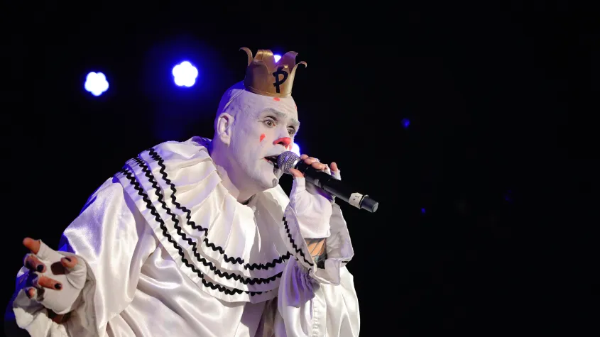 A concert photo of a clown singing on stage. 