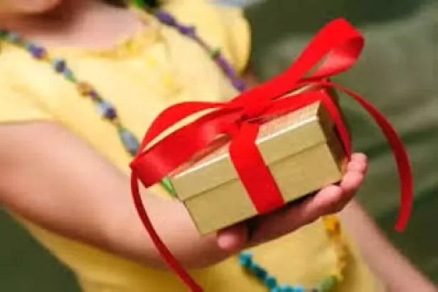 a child in a yellow shirt holding out a wrapped gift in gold paper and a red bow
