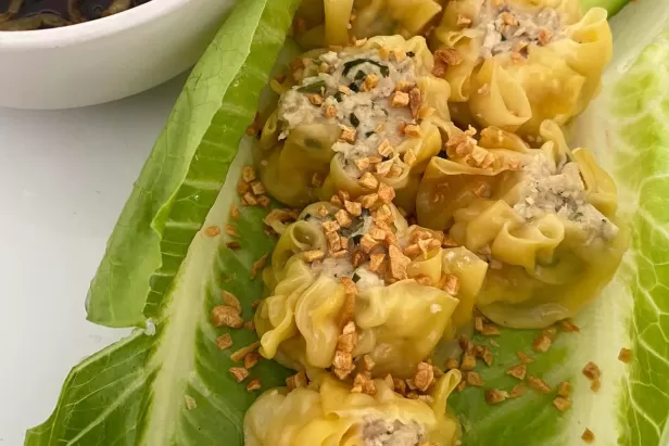image of dumplings on lettuce leaves with seasoning on top and soy sauce in a dish
