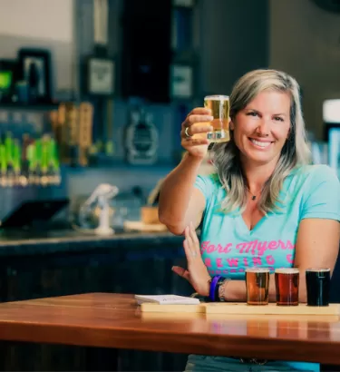 A woman holds a 5oz craft beer pour to cheers the camera