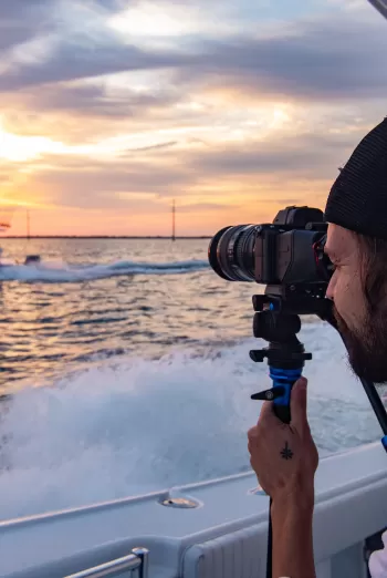 hombre tomando fotos de un barco al atardecer