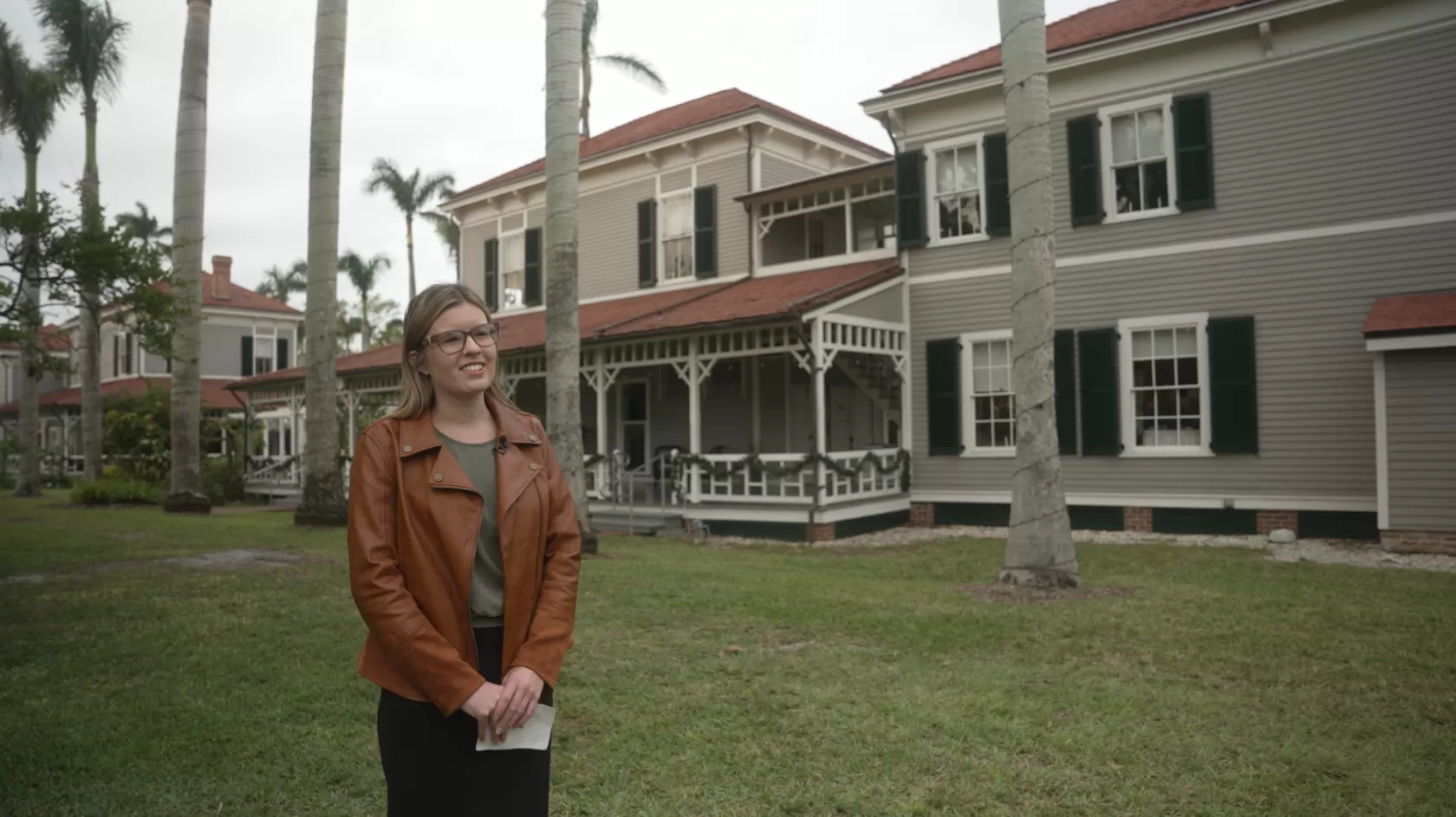 A woman holding a photo stands in front of the historic Edison home in Fort Myers