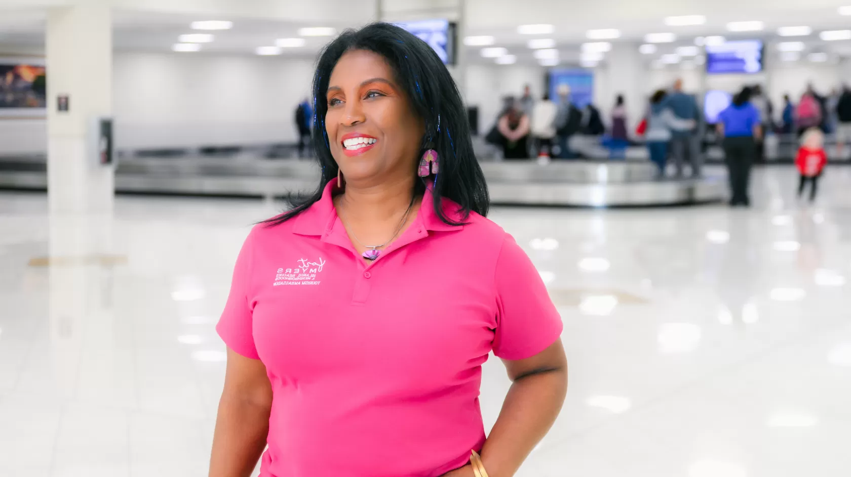 A woman wears a pink shirt and poses near baggage claim at RSW
