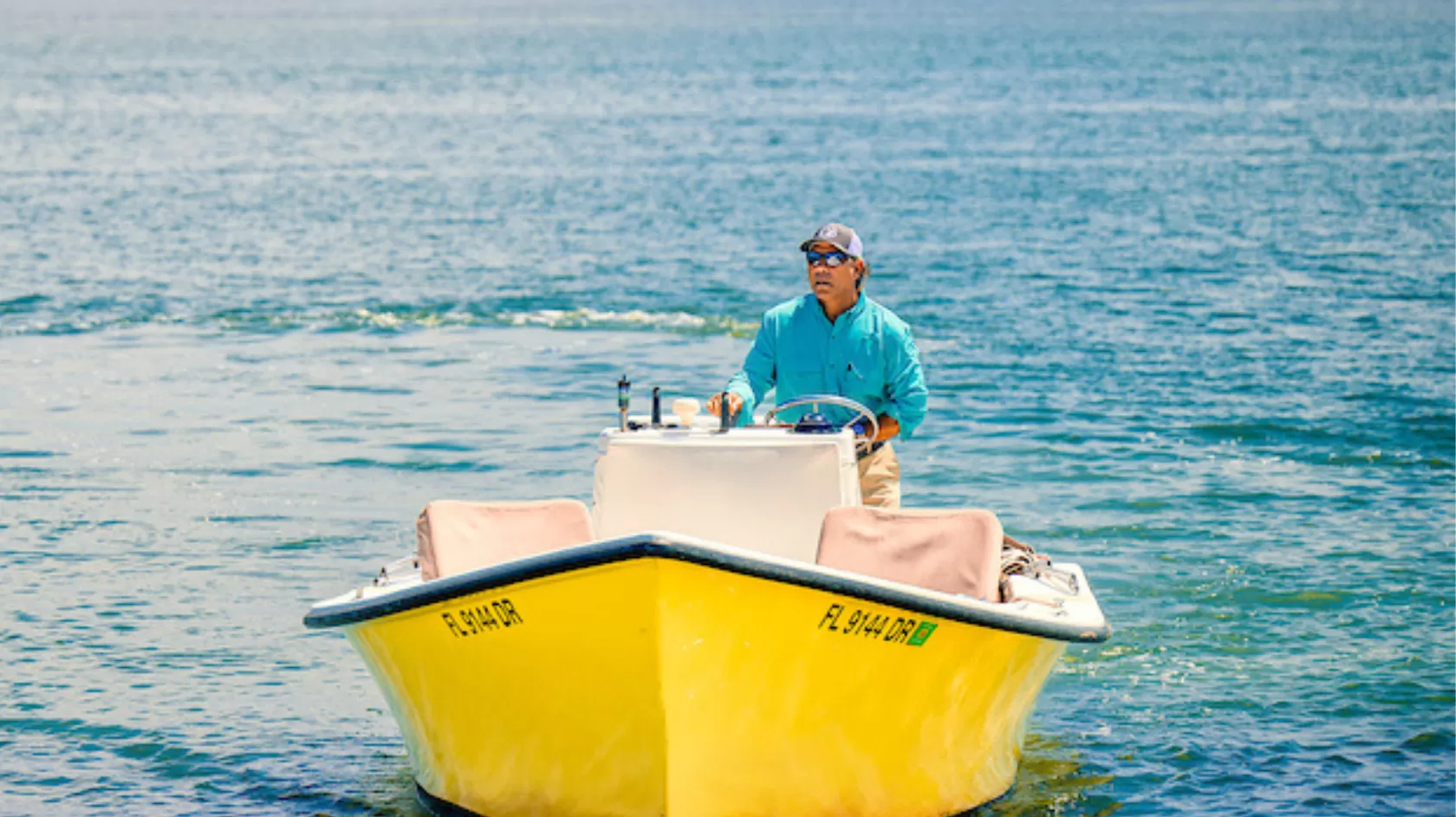 a boat captain drives his boat through calm waters and away from a distant island