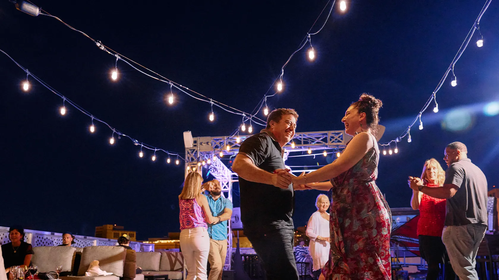 Couple dances salsa beneath string lights.