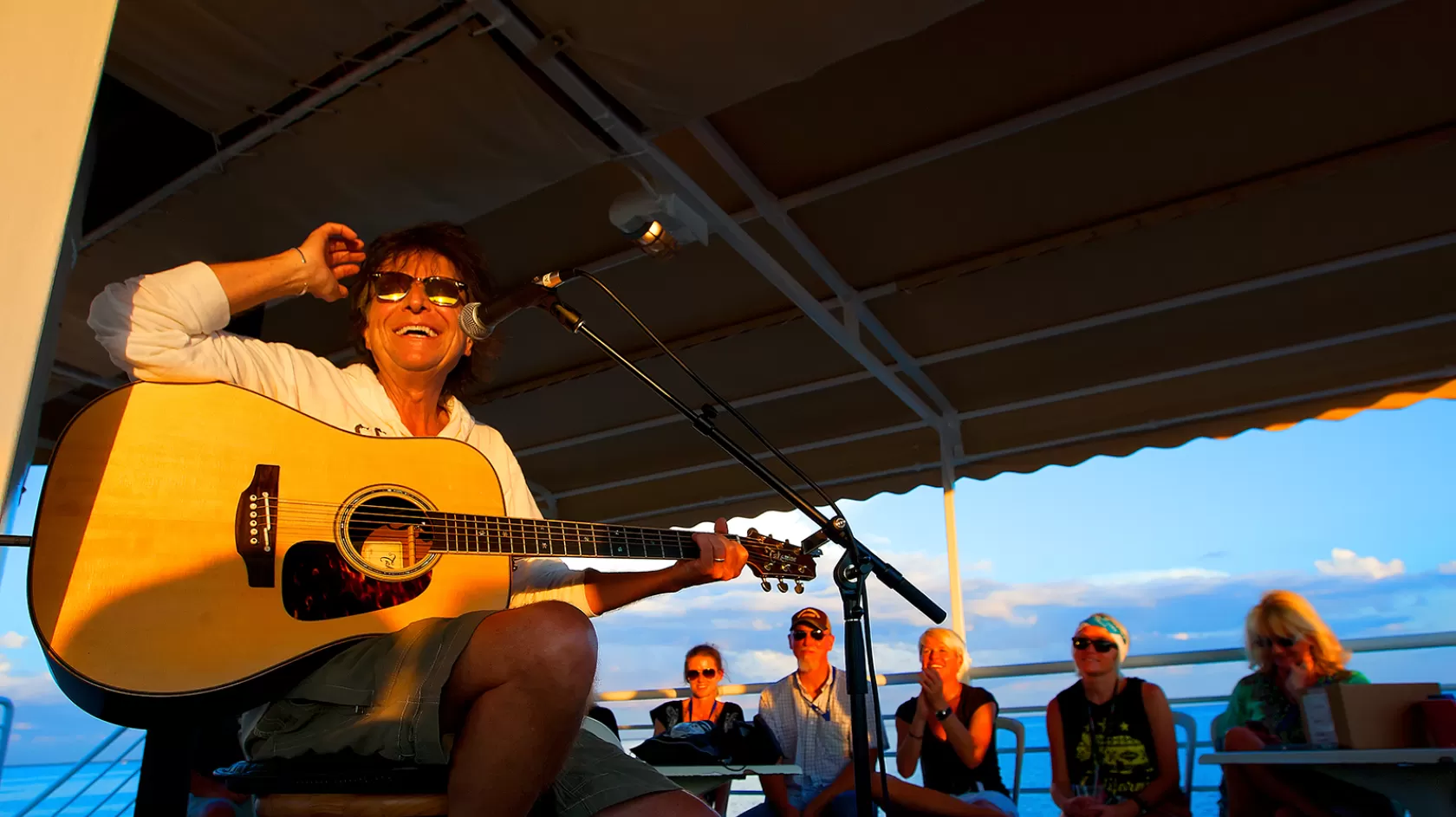 Man playing the guitar for people next to the ocean