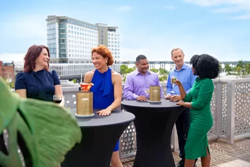 Gruppe auf dem Dach, die Getränke an einem hohen Tisch mit Blick auf das Luminary Hotel in der Innenstadt von Fort Myers genießt