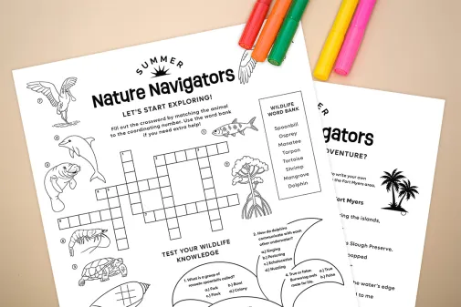 Printed Nature Navigators activity sheets with a crossword, wildlife words and colored markers on a tabletop.