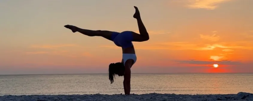 A woman does yoga on the beach at sunset