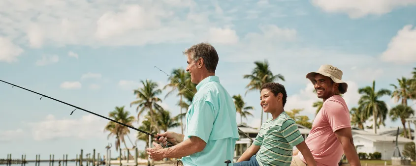 Three people fish together from a dock in Matlacha with palm trees and waterfront homes behind them.