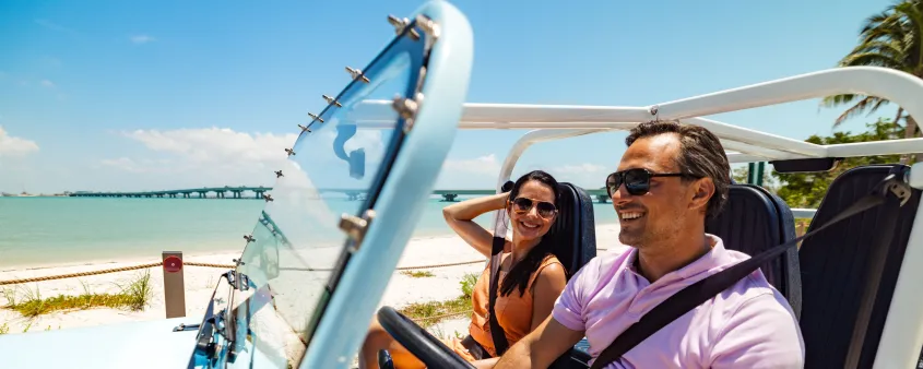 A smiling couple rides in an open-air Moke along the coast of Sanibel.