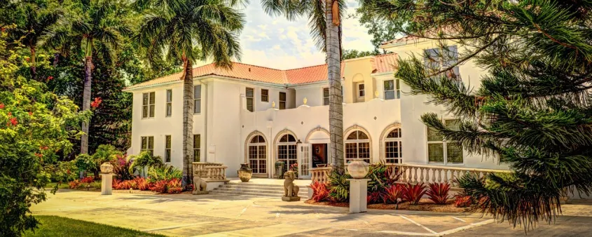 The white stucco Shangri-La Springs hotel stands among palm trees and tropical landscaping in Bonita Springs.