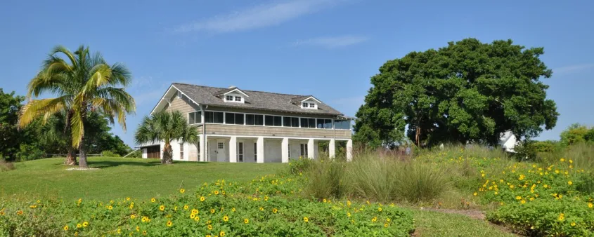 The historic Mound House stands behind native coastal landscaping under a blue sky in Fort Myers Beach.