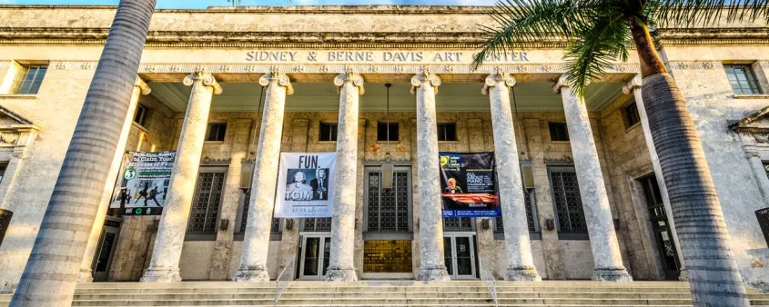 The columned facade of the Sidney & Berne Davis Art Center stands beneath palm trees and a bright blue sky in downtown Fort Myers.