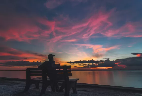 hombre sentado en un banco en Fort Myers mirando el atardecer