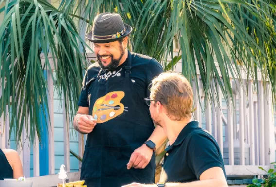 A person serves food to a couple at an outdoor picnic table 