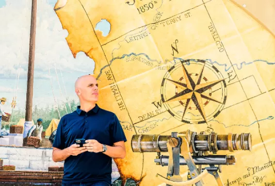 A man stands in front of a painted map mural