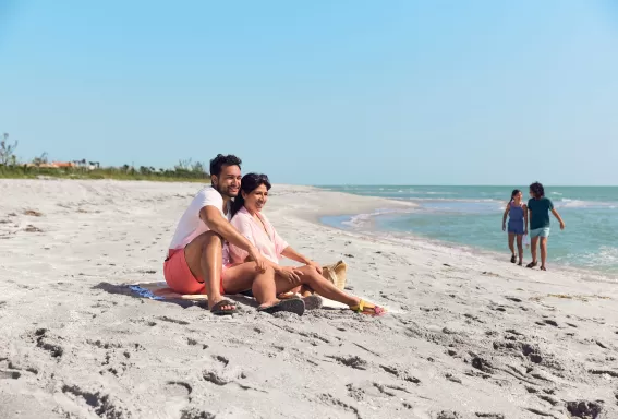 Una pareja sentada en la cima de una playa de arena con niños al fondo