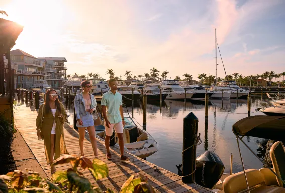 People walk along a marina dock at sunset.