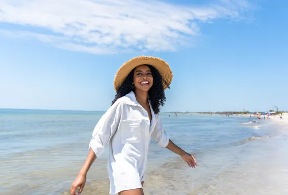 Woman in a straw hat walking through shallow water on a Sanibel Island beach