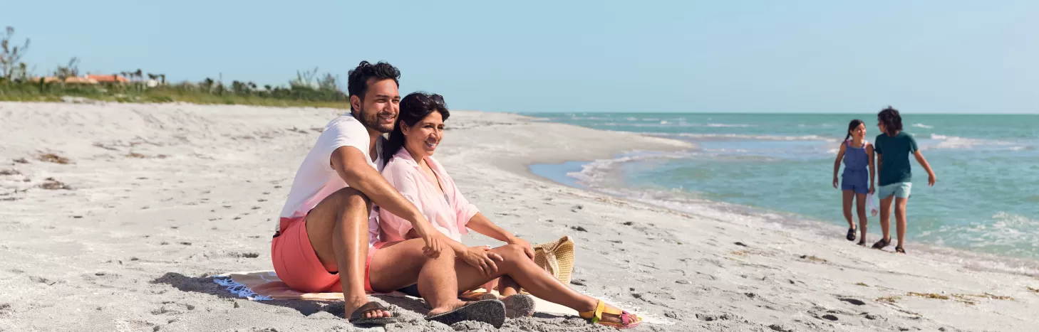 Пара сидить на вершині піщаного пляжу з дітьми у фоновому режимі