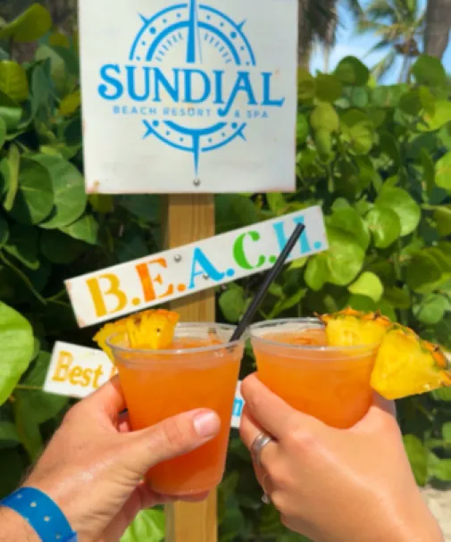 A couple toasts tropical drinks on the beach at Sundial Beach Resort & Spa 