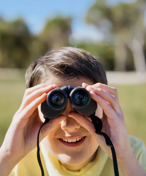 Child looking through binoculars while exploring outdoors.