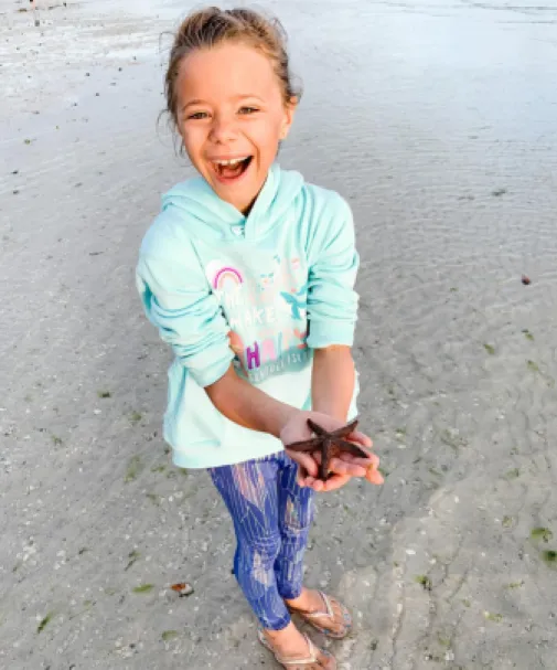 A girl holds a starfish on the beach
