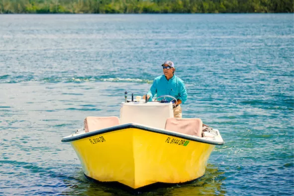 a boat captain drives his boat through calm waters and away from a distant island