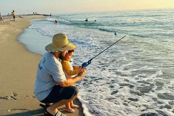 Dad and son fish on the beach.