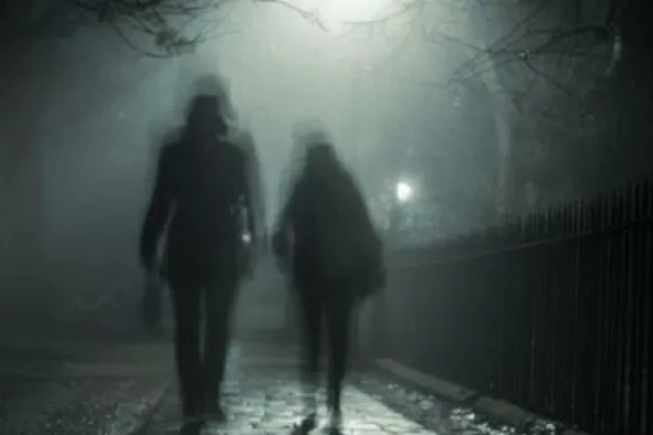 Shadowy figures walk along a brick-paved street looking like ghosts