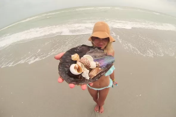 A teenage girl stands on beach and holds shells up