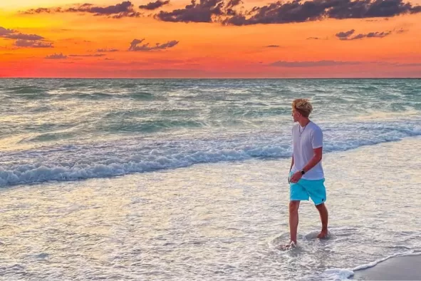 A teen walks along the beach at sunset
