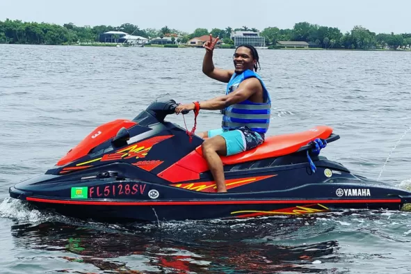 A black man waves from his jet ski on the water