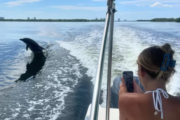 A teen girl takes a picture of a dolphin jumping in the wake of the boat