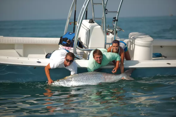 Three people on a boat show off their prize Tarpon