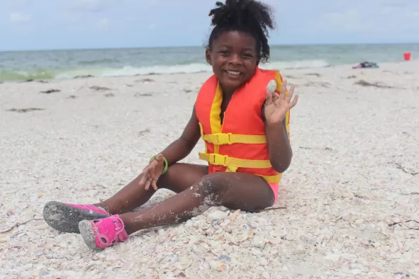 A little black girl sits on the beach collecting shells
