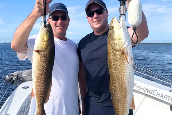 Two brothers hold up their prize catches from their deep-sea fishing adventure