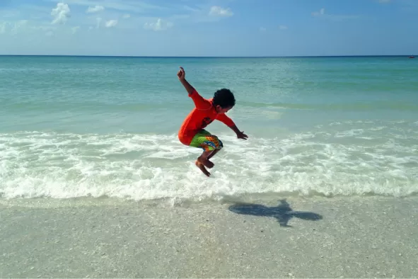 A boy jumps in delight on the beach
