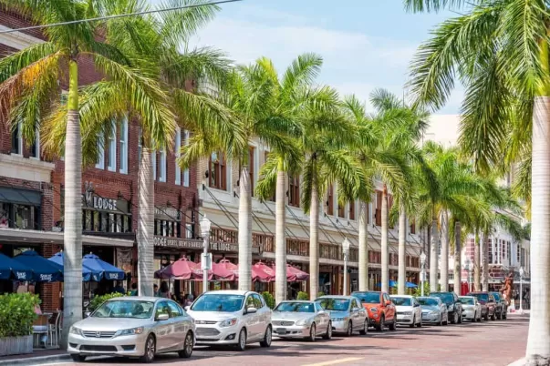 Picture of businesses, cars parked on first street and palm trees in downtown Fort Myers